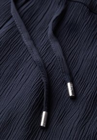 Tissu texturé bleu marine avec de subtiles plis, comportant deux cordons de serrage avec des embouts en métal argenté. Le matériau semble doux et léger.