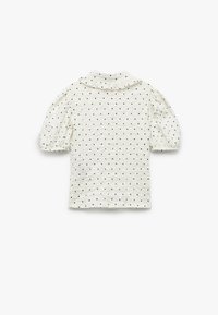 Top blanco de manga corta con un collar con volantes y lunares negros, que presenta mangas abullonadas y una tela texturizada.