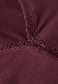 Burgundinen kangas, jossa on sileä pinta, jossa on aktiiviset ompeleet saumoissa ja hieman rypytystä.