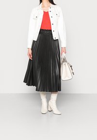 Gonna a pieghe in finta pelle nera, top rosso, giacca in denim bianca e stivali bianchi con tacco. Tiene una borsa color crema con dettagli neri.