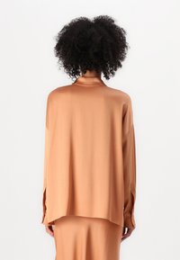 Blusa de manga larga en suave tejido melocotón, con un corte relajado, cuello puntiagudo y discretas aberturas laterales para mayor comodidad al moverse.
