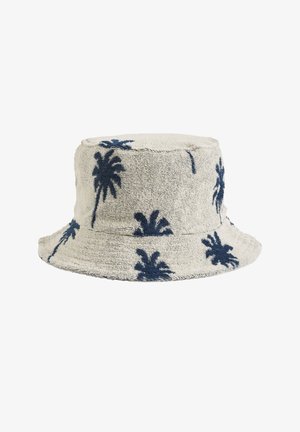 Sombrero tipo bucket elaborado con una tela beige texturizada, con patrones de palmeras en azul marino. Parte superior redondeada, ala ancha y diseño casual.