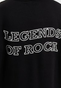 Sort sweatshirt med teksten "LEGENDS OF ROCA" i fed hvid skrift tværs over ryggen, med en blød tekstur og løs pasform.