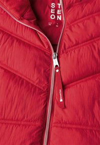  närbild av röd vadderad jacka dragkedja med tygdragpull, märkt "Street One" och tryckta storleksdetaljer inuti.