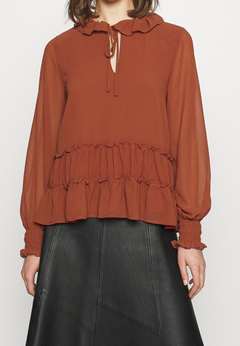 Rostfärgad blus med volangkrage och fåll, med långa ärmar med smockade manschetter och en nyckelhålsdetalj vid halsen.