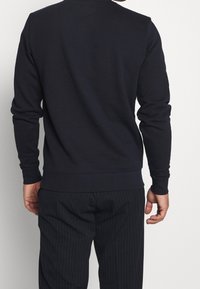 Sudadera de algodón en color navy con mangas largas, cuello redondo y puños acanalados. Presenta un diseño liso sin logotipos ni patrones visibles.