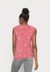 Blusa sem mangas cor de rosa com um padrão floral e borboletas em azul e branco, parte traseira texturizada com pregas e um pequeno detalhe de logótipo.