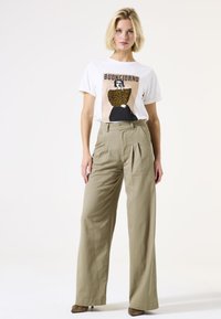 T-shirt blanc avec un graphique "Buongiorno" et un design à imprimé léopard, associé à un pantalon beige taille haute à jambes larges et des talons texturés.