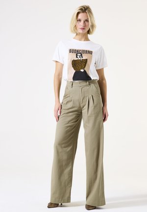 T-shirt blanc avec un graphique "Buongiorno" et un design à imprimé léopard, associé à un pantalon beige taille haute à jambes larges et des talons texturés.