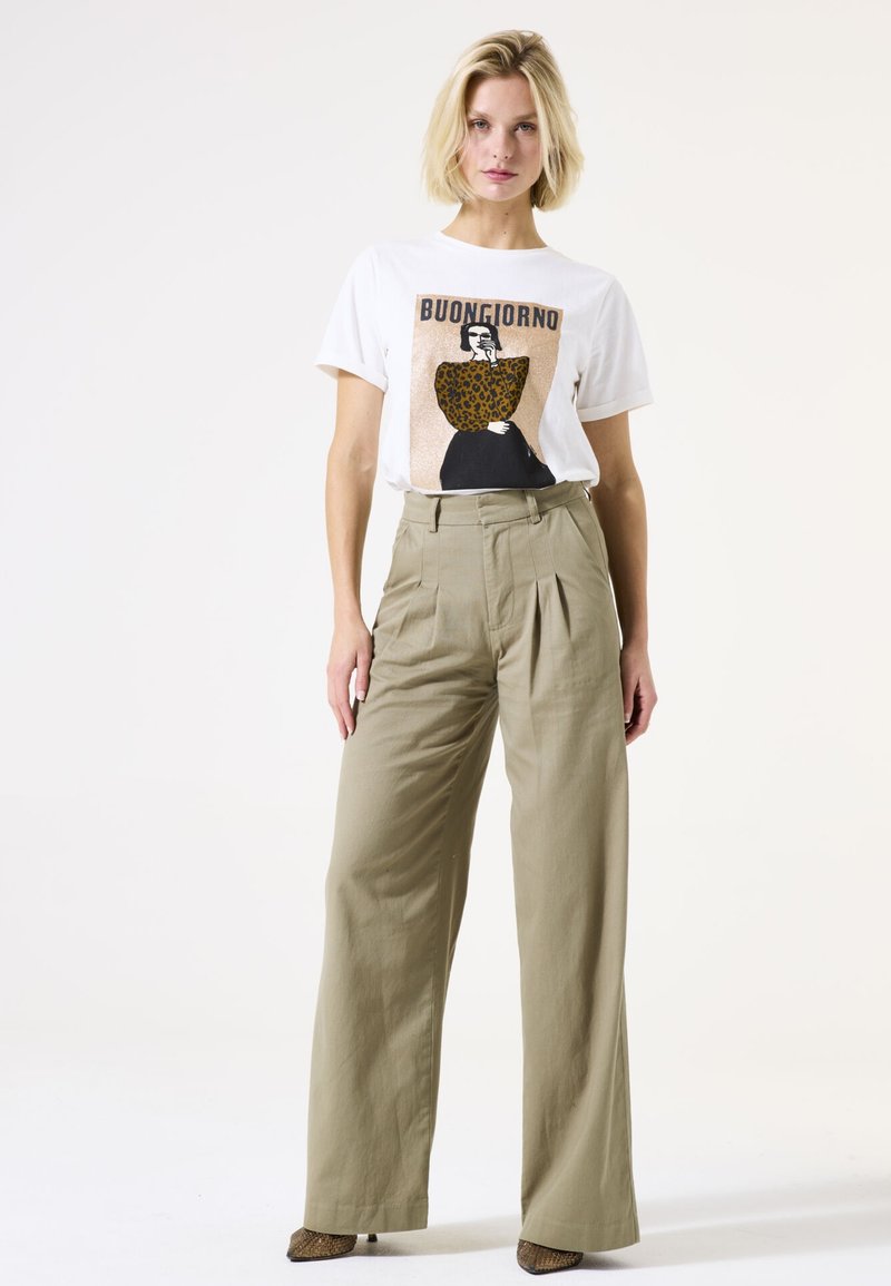 T-shirt blanc avec un graphique "Buongiorno" et un design à imprimé léopard, associé à un pantalon beige taille haute à jambes larges et des talons texturés.