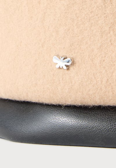 Gros plan sur une surface en feutre beige avec une petite épingle argentée en forme d’insecte au-dessus d’une bordure en cuir noir.