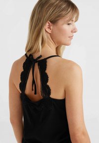 Svart ärmlös topp med en scallop-lace baksida och knytning. Tillverkad av mjukt tyg har den en figurnära silhuett och subtil textur.
