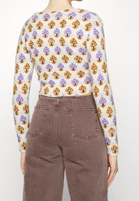 Krämfärgad tröja med mönster av lila och bruna svampar, långärmad, figursydd design, kombinerad med bruna högmidjade byxor med bakfickor.