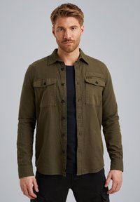 Camicia verde oliva a maniche lunghe in tessuto texturizzato. Presenta due tasche sul petto con pattine, un'etichetta nera sul lato destro e una vestibilità comoda.