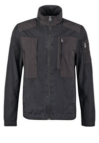 Giacca nera con colletto alto, chiusura con zip e numerose tasche. Tessuto composito con una texture liscia e pannelli sulle spalle in contrasto.