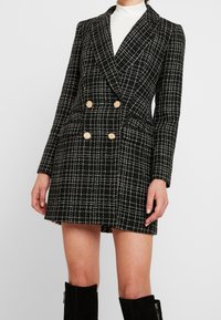 Black and white checkered blazer dress, double-breasted with gold buttons, structured fabric, notched lapels, and side pockets.