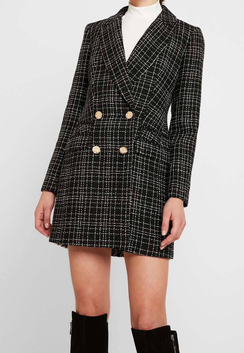 Black and white checkered blazer dress, double-breasted with gold buttons, structured fabric, notched lapels, and side pockets.