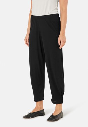 Zwarte trainingsbroek met een elastische tailleband, taps toelopende benen en bijeen geraapte manchetten. Draagt met zwarte flats en een lichtgekleurde, aansluitende top.