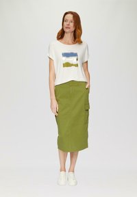 T-shirt blanc avec un design abstrait multicolore, associé à une jupe olive verte longueur genoux avec des poches cargo et une coupe droite.
