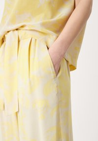 Yellow floral-patterned blouse paired with matching trousers, featuring soft fabric, pleats, and side pockets, creating a cohesive outfit.