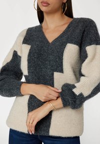 Maglione color bloc grigio e crema in morbido materiale a maglia con scollatura a V e polsini a coste. Presenta una vestibilità comoda e dettagli a strisce.