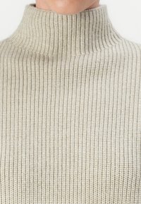 Maglione a collo alto ribbed beige con un collo alto e un motivo a maglia testurizzato. Materiale morbido, design aderente.