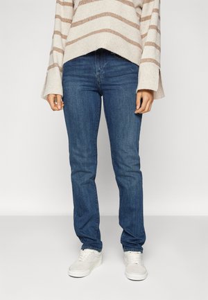 Jeans de mezclilla azul con un corte recto, con un lavado medio y un ligero desgaste. Combinados con un suéter de rayas claras y zapatillas blancas.