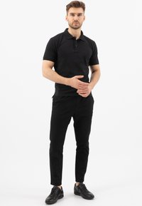 Černé polo tričko s límečkem, krátkými rukávy a zapínáním na tři knoflíky; v kombinaci s černými slim-fit kalhotami a černými teniskami.