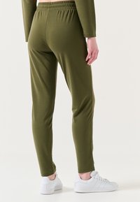 Olijfgroene, aansluitende broek met een gladde textuur en een elastische tailleband; gecombineerd met witte sneakers voor contrast.