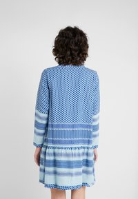 Sininen ja vaaleansininen kuvioitu rento mekko, jossa on pitkät hihat, kerrostettu helma, geometrisia kuvioita ja vaihtelevaa tekstuuria kankaassa.