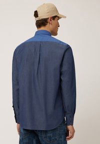 Blue long-sleeve shirt with a contrasting lighter blue collar. Made of lightweight fabric, features a back pleat, and button cuffs.