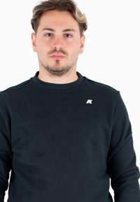Czarna bluza z długim rękawem, wykonana z prążkowanego materiału, z okrągłym dekoltem i małym, odblaskowym logo na lewej piersi.
