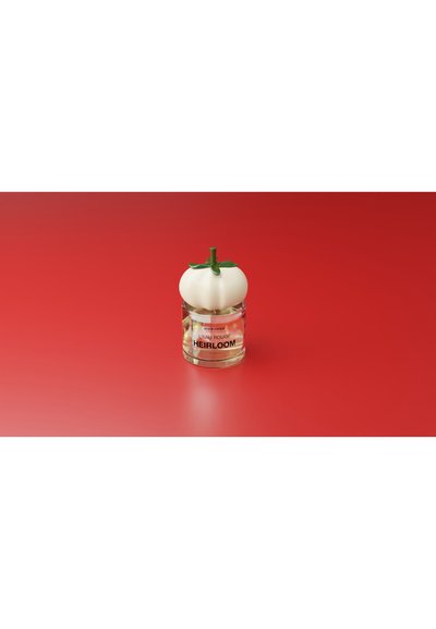 Genomskinlig glasparfymflaska med vit tomatlika kork på röd yta, märkt "L'eau Rouge Heirloom" av Henrik Vibskov.