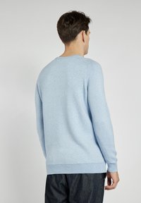 Helles blauer Rundhals-Pullover mit gerippter Textur, langen Ärmeln und lockerer Passform. Abgeschlossen mit einem schlichten Saum und Bündchen.