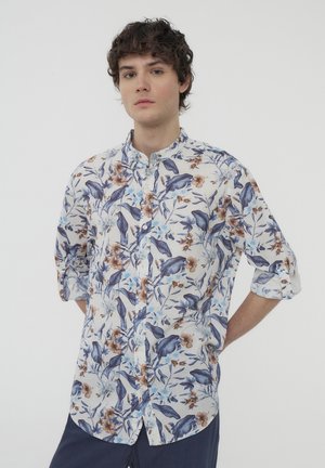 Camicia a maniche corte con bottoni, caratterizzata da fantasie blu e marroni su sfondo bianco, con colletto alla coreana e maniche arrotolate.