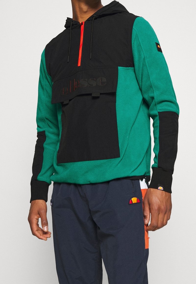 Felpa con cappuccio verde e nera, con zip frontale, patch del logo e tessuto texturizzato; presenta maniche nere a contrasto e zip rossa.