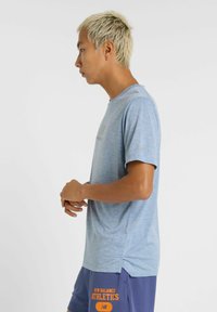 Camiseta deportiva azul claro con cuello redondo, mangas cortas y aberturas laterales. Presenta un branding minimalista en un tono más oscuro.