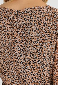 Tissu imprimé léopard aux tons chauds de beige et de marron avec des accents noirs. Présente un col rond et une fermeture éclair au dos.