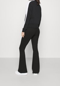 Sort zip-up hættejakke med hvide sidestriber, parret med sorte flared bukser og hvide sneakers. Glat stof med en tætsiddende silhuet.