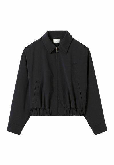 Chaqueta negra corta de tejido suave, con cierre frontal, gran solapa y cinturilla elástica con bolsillos laterales.