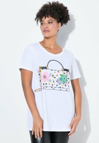 Witte t-shirt met een grafisch ontwerp van een handtas met bloemenpatronen in roze, groen en blauw, verfraaid met gouden en zwarte details.