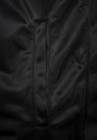 Černá látka s hladkým, texturovaným povrchem a vertikálním rozparkem uprostřed, orámovaným prošíváním podél okrajů.