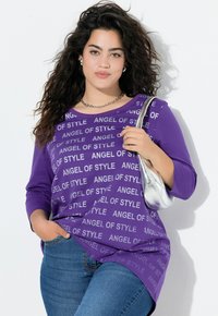 Camicetta viola con il testo "ANGEL OF STYLE" in bianco, scollo rotondo, maniche a 3/4. Indossata con jeans blu e una borsa a spalla argento.