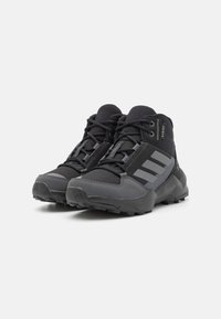 Black and grey outdoor shoes with a textured upper, featuring three vertical stripes, reinforced toes, and a rugged sole for traction.
