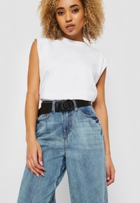 Top blanco sin mangas combinado con pantalones vaqueros de mezclilla azul de cintura alta y un cinturón negro con hebilla circular. Tejido suave, corte relajado.
