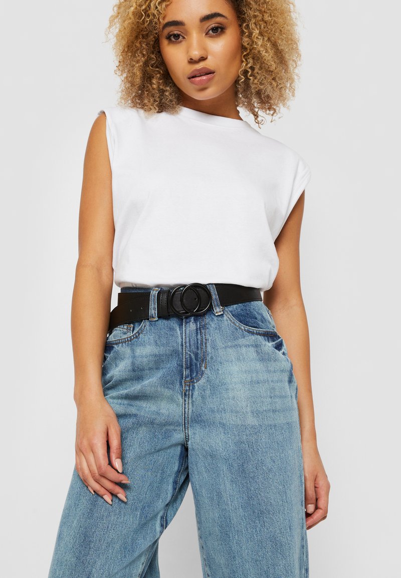 Top blanco sin mangas combinado con pantalones vaqueros de mezclilla azul de cintura alta y un cinturón negro con hebilla circular. Tejido suave, corte relajado.