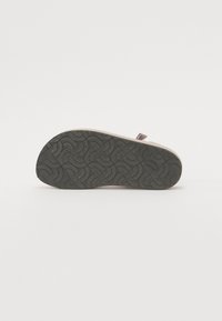Lysfarget sandal med en teksturert gummisåle, med et vevd mønster. Justerbar stropp i mørk farge for sikker passform.