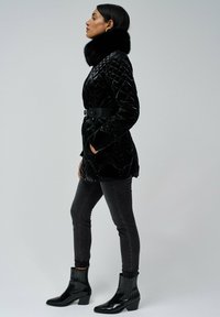 Sort kviltet frakke med pelskrave, belted i taljen, parret med mørke skinny jeans og blanke sorte ankelstøvler med tekstureret finish.