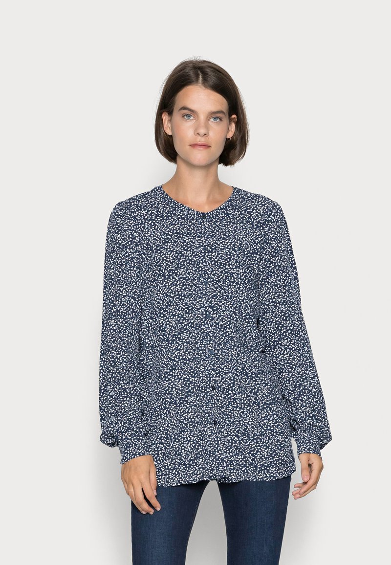 Blusa azul-marinho com padrão salpicado branco, mangas longas e decote redondo. O tecido tem uma textura suave e um corte descontraído, combinada com jeans escuros.