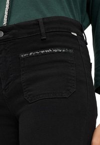 Jeans in denim nero con una tasca posteriore decorata da una sottile striscia di paillettes nere, con una finitura testurizzata e il classico design a cinque tasche.